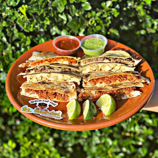 A platter of El Rucon's Mexican quesadillas with various fillings, lime wedges, and two dipping sauces.