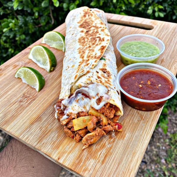El Rucon's large burrito with melted cheese, limes, and two dipping sauces on a wooden board.