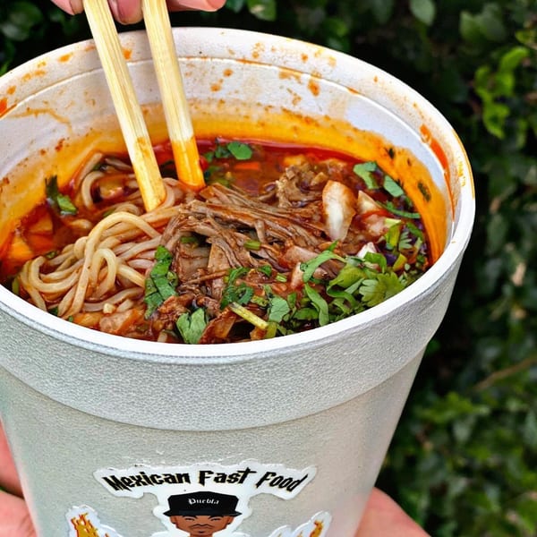 Chopsticks in a styrofoam cup of El Rucon's birria ramen with shredded meat and cilantro.