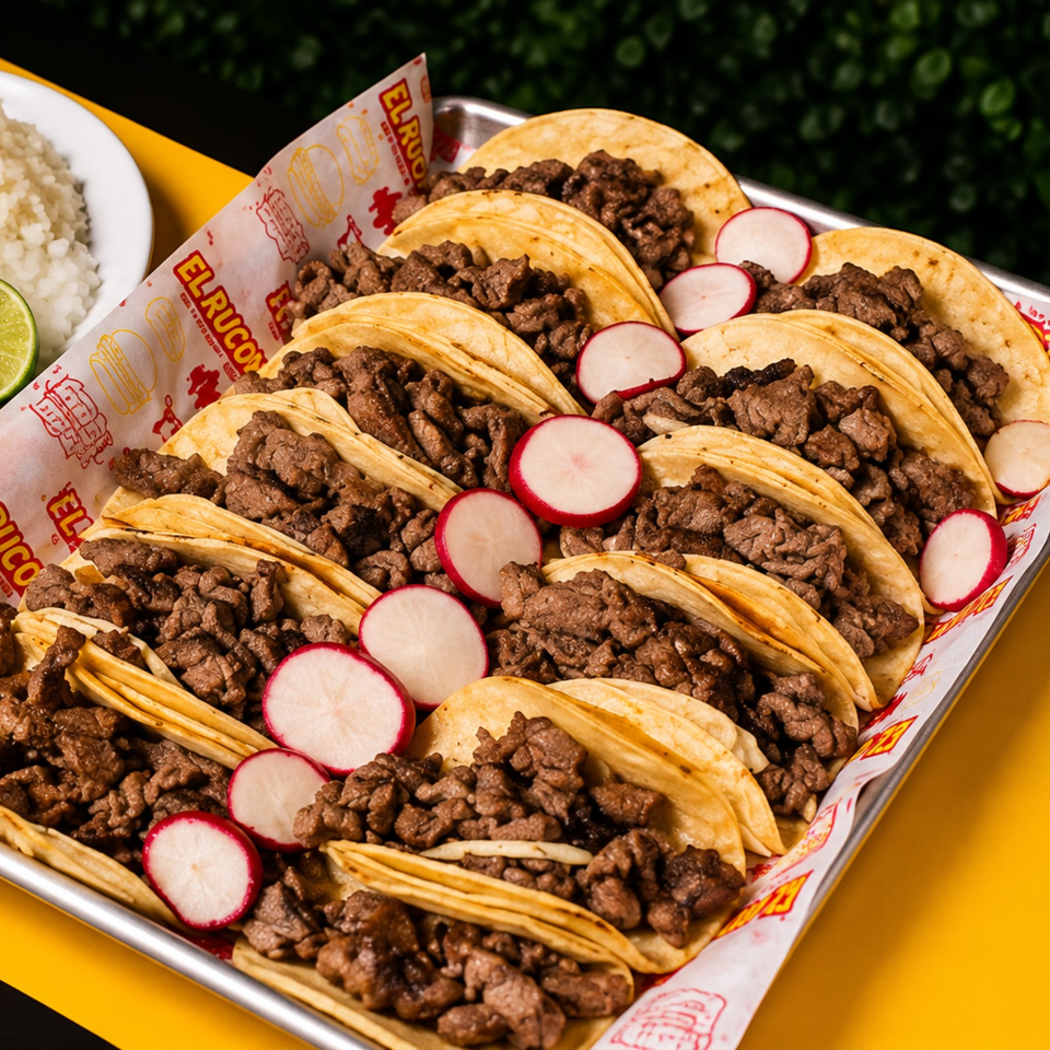 Tray of small corn tortillas filled with grilled beef and garnished with sliced radishes, lime, and rice.